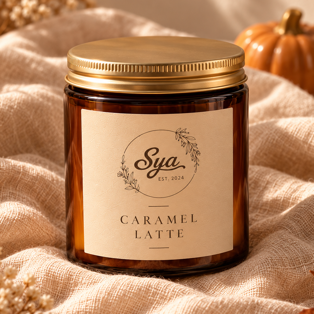 Caramel Latte candle in an amber glass jar with a gold lid, resting on beige fabric.