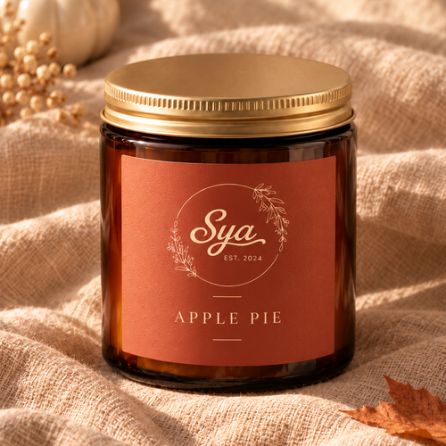 Apple Pie candle in an amber glass jar with a gold lid, resting on beige fabric.