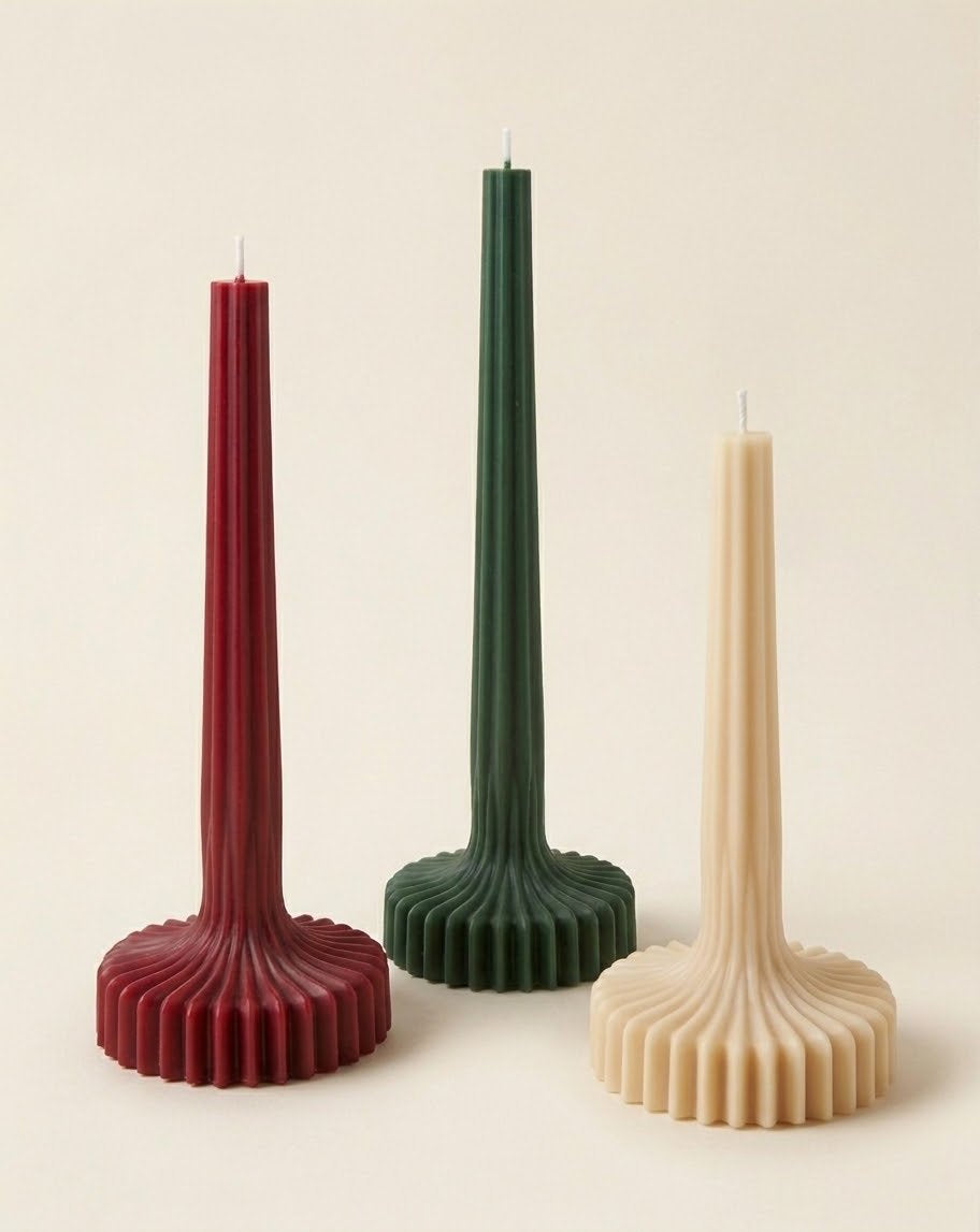 Red, green and beige Bloom Elegance candles with tall ribbed stems and fluted round bases.