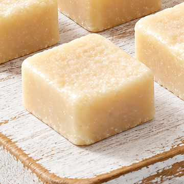 Close-up of cream-colored, square Dulce de Leche wax melts on a pale wooden board.